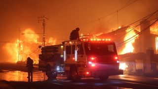 Firefighters and a fire truck in front of burning houses during Palisades Fire 2025